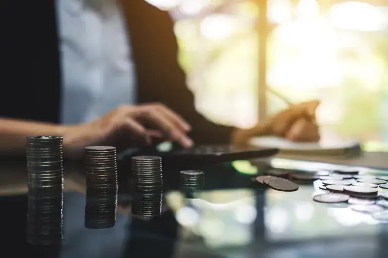 An image of a woman working on a tablet, with coins stacked up on the table