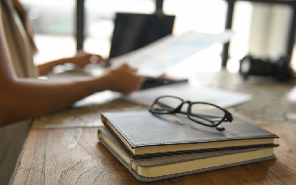 An individual reading through documents next to some books and glasses.