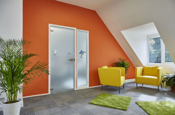 Office Meeting Room an orange wall and glass door with Innovation Visual logo and yellow chairs.