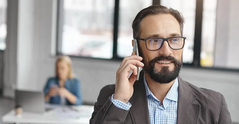 business man smiling on phone working collaboratively with digital agency with colleague in background